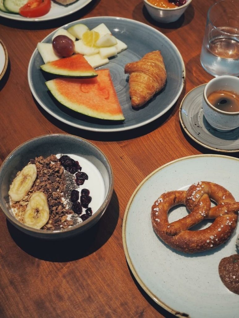 Gedeckter Frühstückstisch mit gesundem Müsli, Brezeln, Obst und Espresso