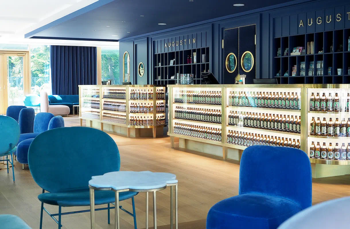 Elegante Lobby des Augustin Hotels mit blauem Interieur, beleuchteten Bierregalen und einem einladenden Sitzbereich.