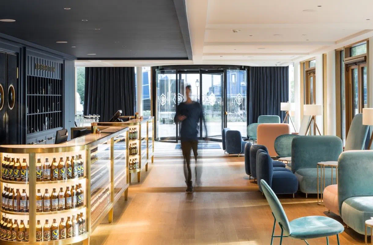Moderne Lobby des Augustin Hotels mit beleuchtetem Bierregal, gemütlichen Samtsesseln und einem gläsernen Eingang.