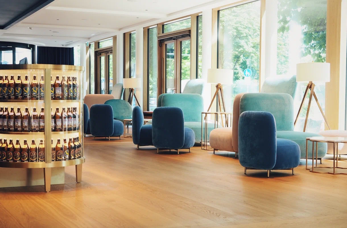 Einladende Lobby des Augustin Hotels mit modernen blauen und rosa Samtsesseln, großen Fenstern und stilvoller Beleuchtung.