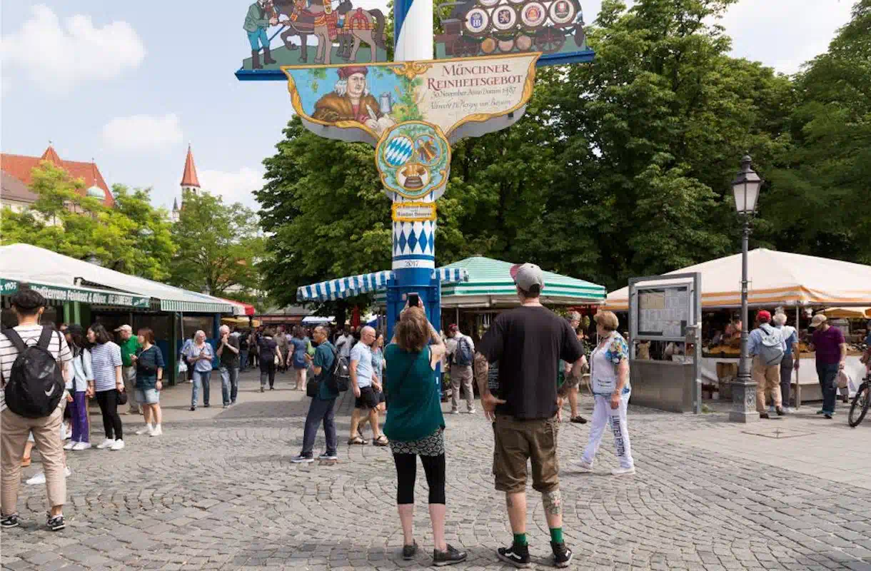 Belebter Viktualienmarkt in München mit Marktständen, Besuchern und dem Maibaum im Vordergrund