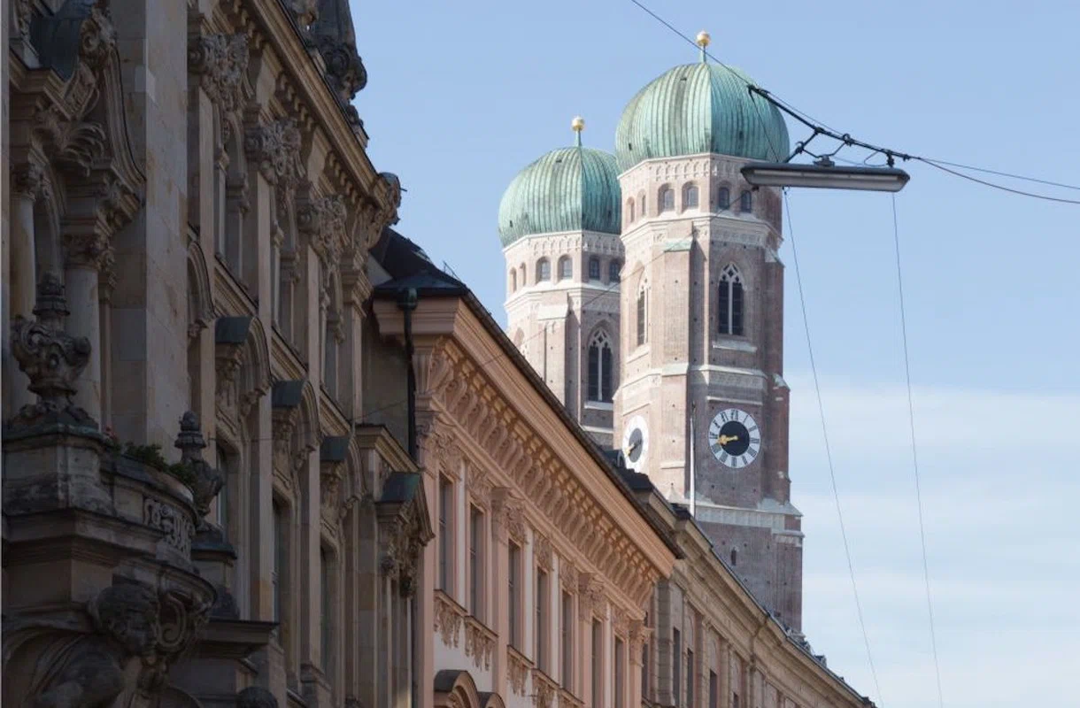 Frauenkirche in München mit ihren markanten Zwiebeltürmen, umgeben von historischen Gebäudefassaden unter blauem Himmel
