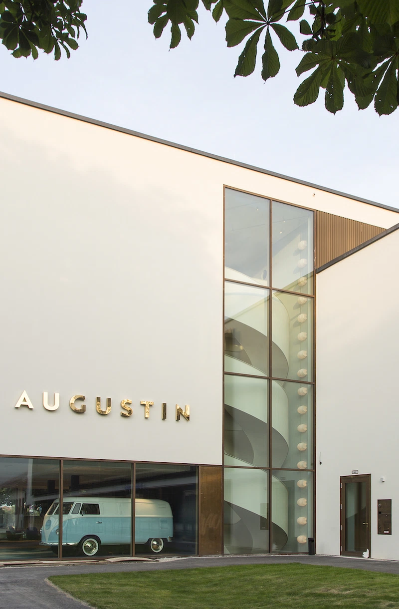 Moderne Fassade des Jugend- und Familienhotel Augustin in München mit einem blauen VW-Bus im Schaufenster und goldfarbenem Hotel-Schriftzug.