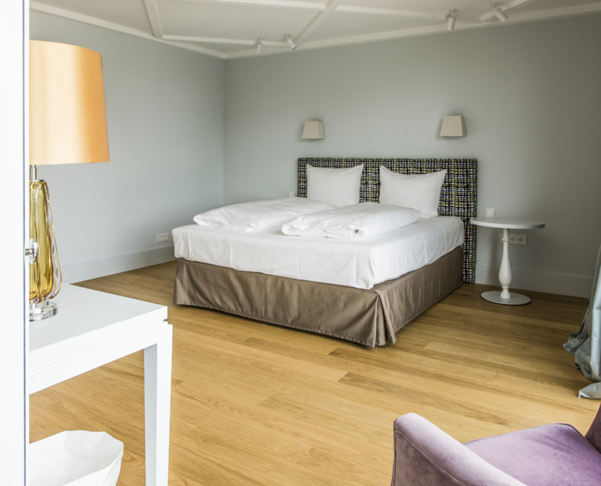 Blick ins geräumige Schlafzimmer mit einem hohen, gemütlichen Doppelbett in blauen Tönen und einem warmen Holzfußboden