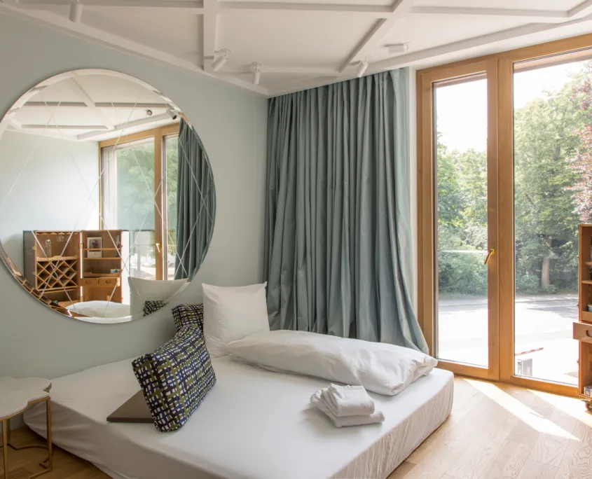 heller Raum mit großer Matratze und rundem Spiegel dahinter